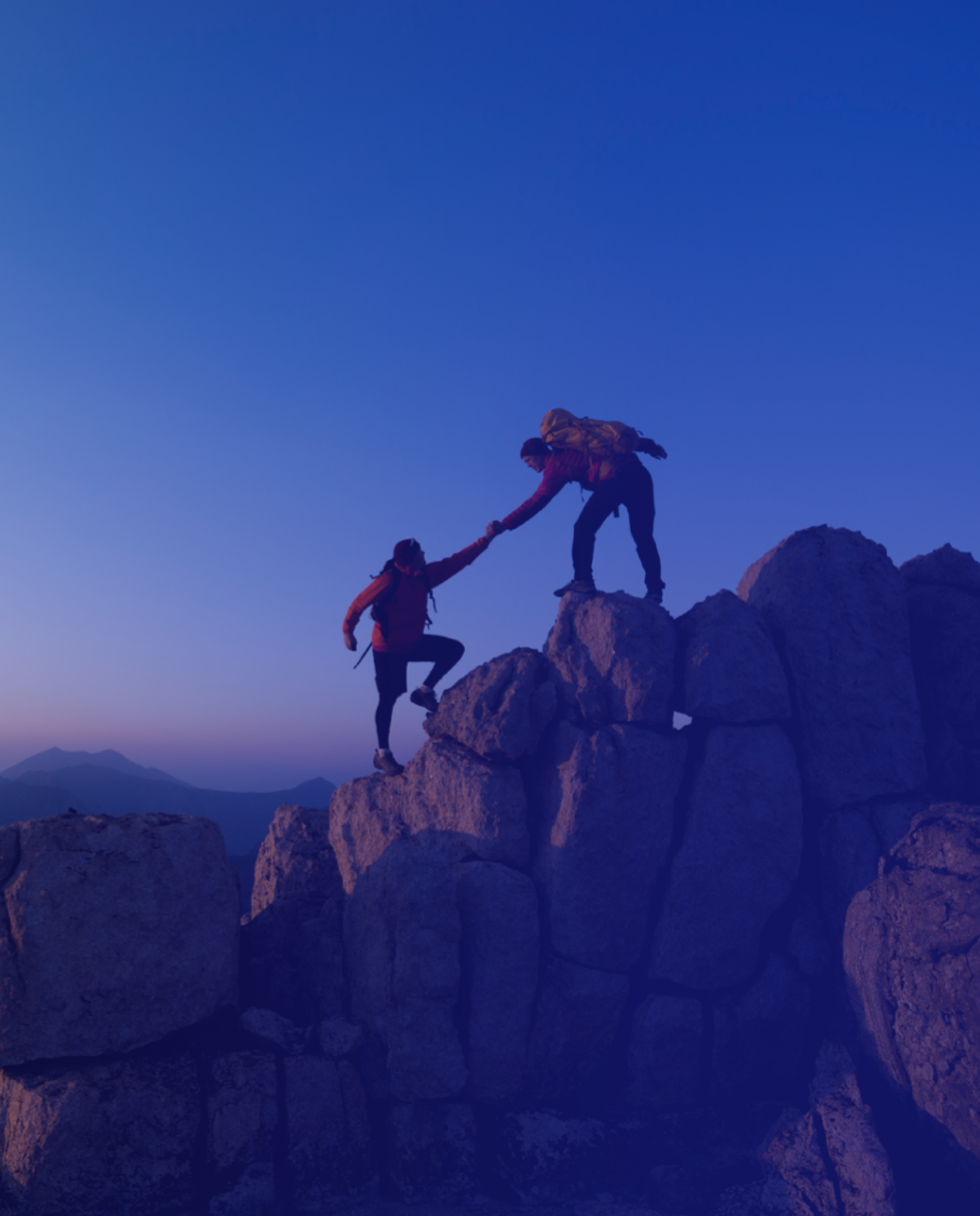 Two rocker climbers on a mountain, one is helping the other climb up a rock